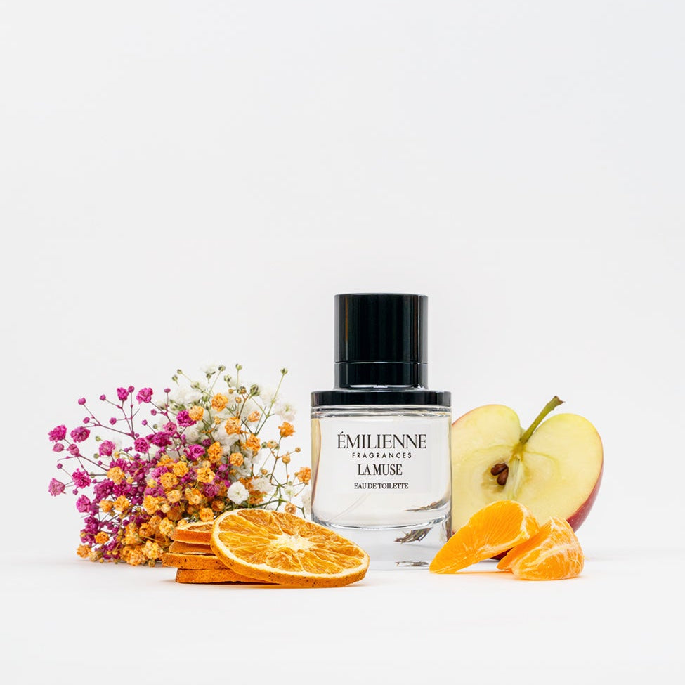 Perfume bottle with flowers, apples, and oranges on a white background